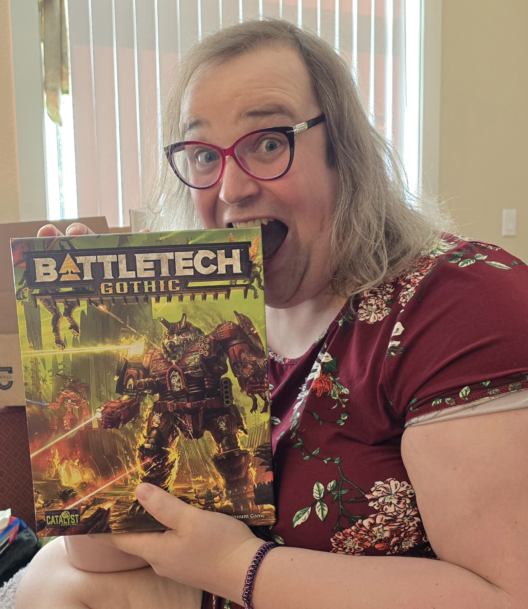 The author, wearing an adorable maroon and floral skater dress, excitedly tests the quality of the BattleTech Gothic box set.